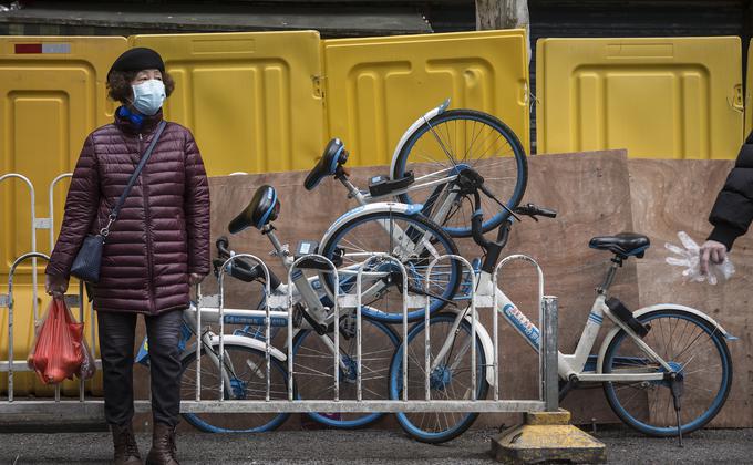 图为武汉一名带着口罩的妇女站在临时路障墙前。 (图片来源:Getty Images)